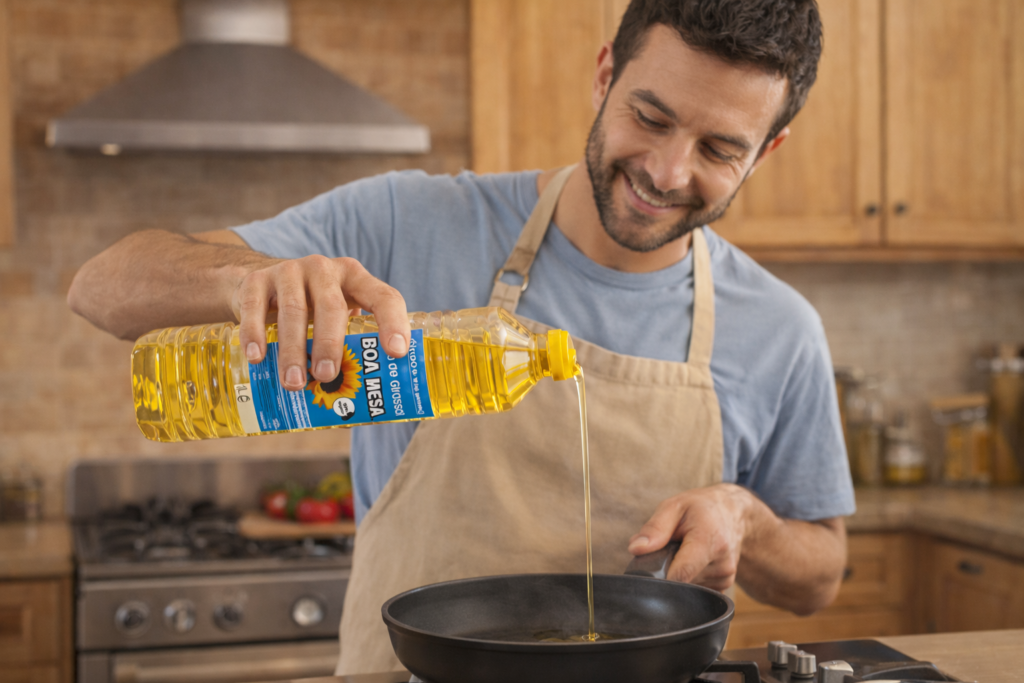 Hombre cocinando en casa mientras vierte aceite de girasol Boa Mesa en una sartén, usando una botella de 1 litro durante la preparación de alimentos.